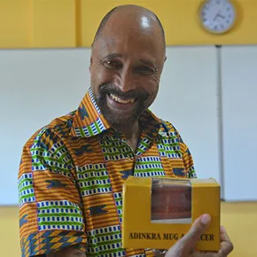 Smiling man in colorful African-print shirt holding a mug.