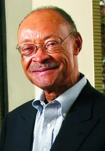 Elderly man in glasses and suit smiling at the camera.
