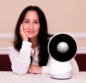 Woman posing with a robotic device on a table.